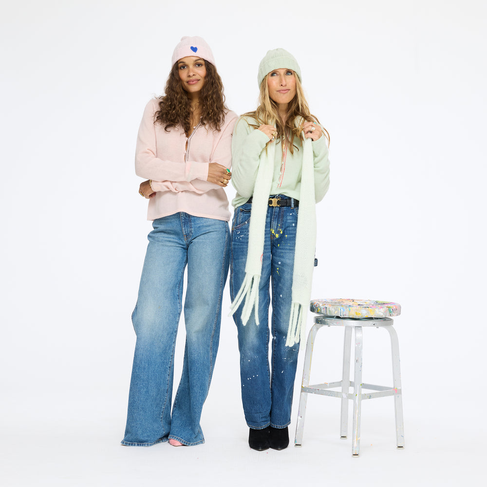 Two women standing beside a stool in wide-leg jeans, one wearing the Winter Beanie in hardly pink with the Pixie Sweater in pink