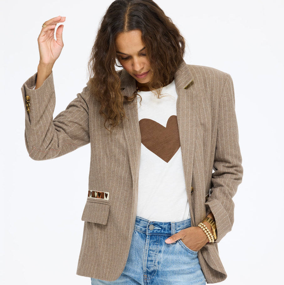 Model wearing the Workday Love Brigade Blazer in taupe over the Long Sleeve Suke Imperfect Heart Tee in cream with a brown heart and jeans, one hand raised