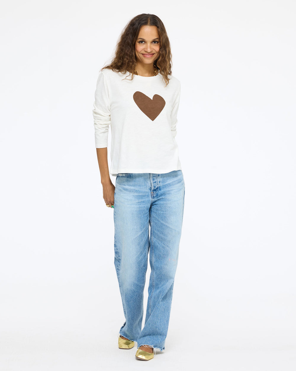 Model wearing the Long Sleeve Suke Imperfect Heart Tee in cream with a brown heart and jeans, full length front view