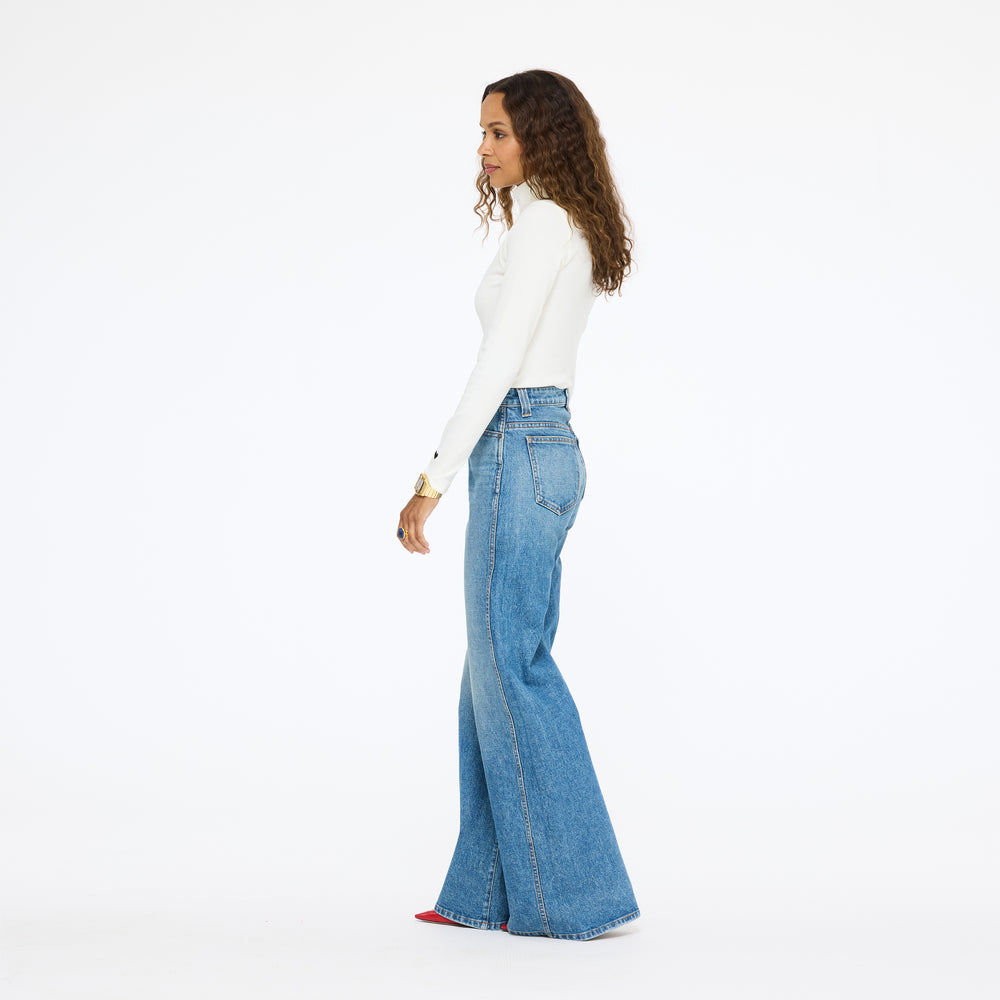 Model wearing the Mock Neck Rib Tee in cream with wide-leg jeans, side view