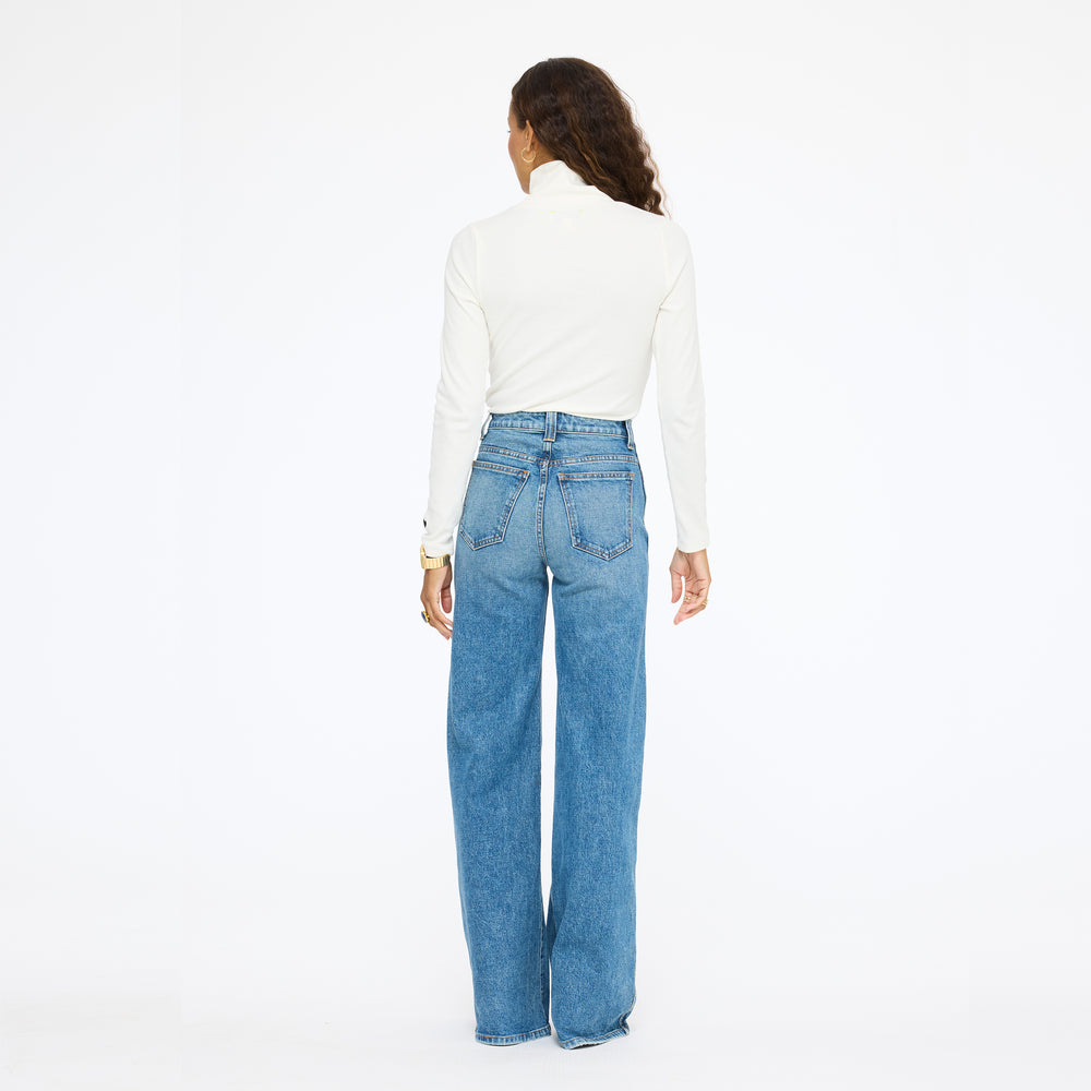 Model wearing the Mock Neck Rib Tee in cream with wide-leg jeans, back view