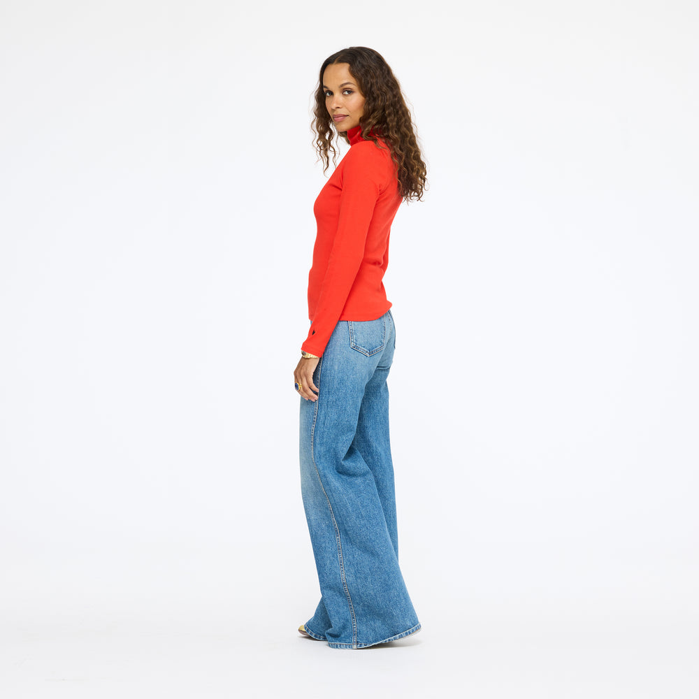 Model wearing the Mock Neck Rib Tee in red with wide-leg jeans, side view
