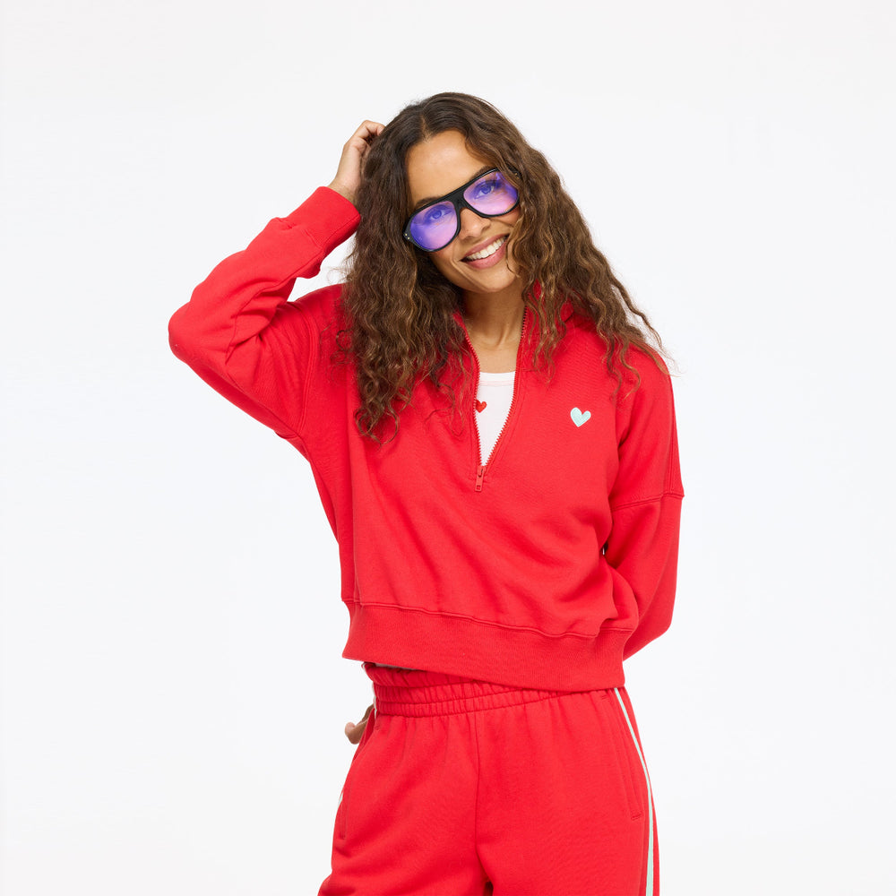 Model wearing the Sunday Quarter Zip Sweatshirt in red with the Super Soft Fleece Weekend Palazzo in red and sunglasses, one hand raised to her head