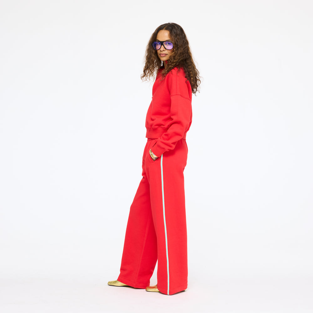 Model wearing the Sunday Quarter Zip Sweatshirt in red with the Super Soft Fleece Weekend Palazzo in red and its white side stripe, full length side view