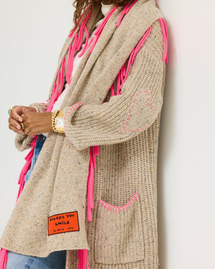 Model wearing the Morning Coffee Duster in oatcake with the Makes You Smile Scarf in oatcake with neon pink fringe, three-quarter view