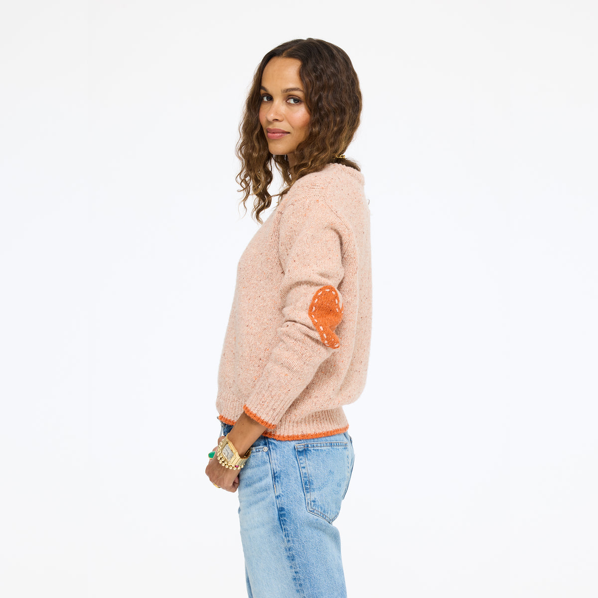Model in side profile wearing the Patchwork Pullover Sweater in blush with orange heart elbow patches and jeans
