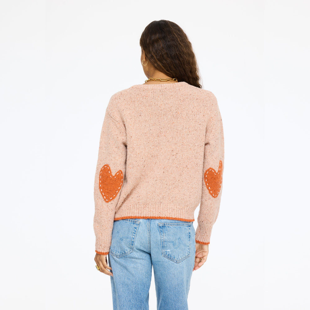 Model wearing the Patchwork Pullover Sweater in blush with jeans, back view showing orange heart elbow patches