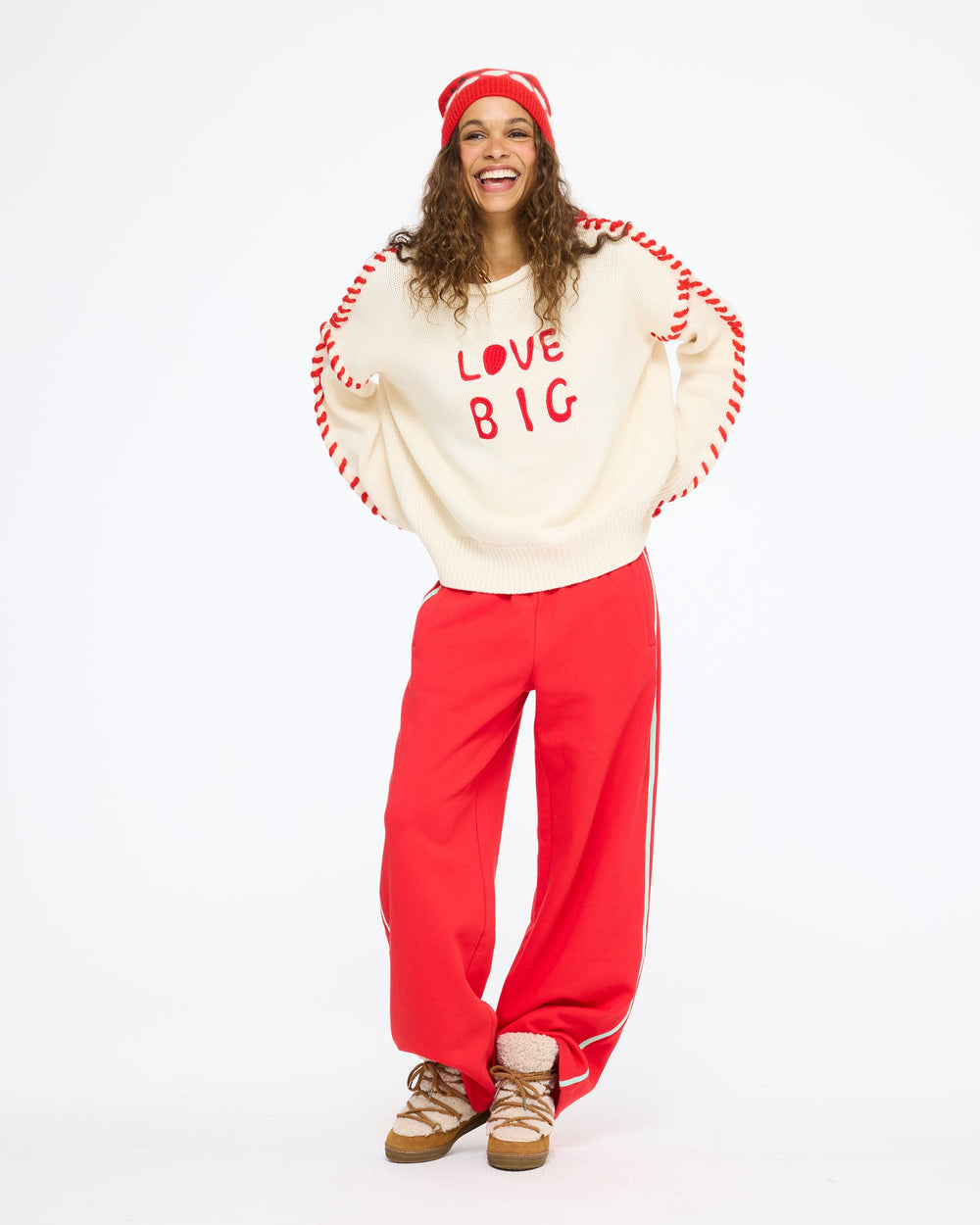 Model wearing the Love Big Sweater in cream with the Super Soft Fleece Weekend Palazzo in red and the Rosey Beanie, hands on hips, full length front view