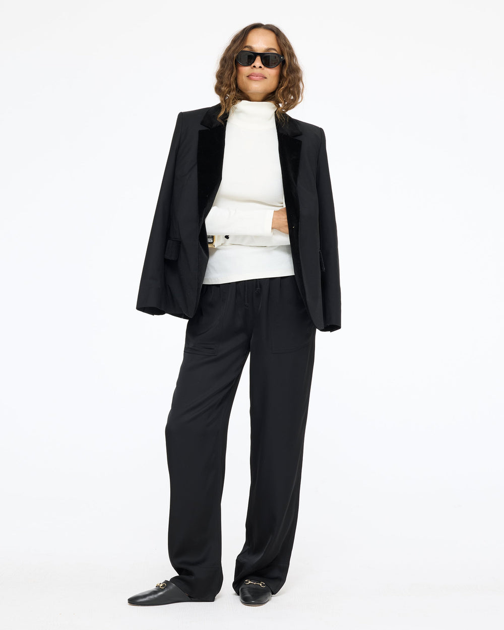 Model wearing the Workday Fancy Blazer in black with the Coast Pant in black, a white turtleneck, and sunglasses, front view
