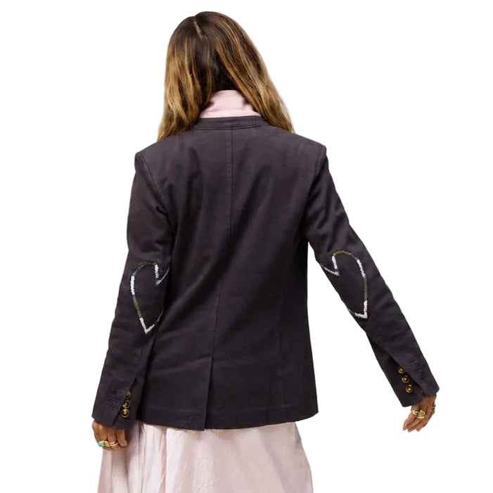 Back view of the Workday Blazer in Anthracite, a structured brown-grey blazer with heart-shaped stitched patches on both sleeves, worn by a woman in a pink maxi skirt. Kerri Rosenthal women's blazers