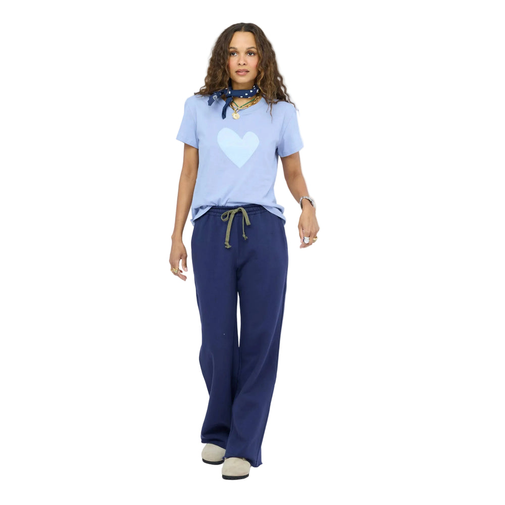 Woman wearing a Kerri Rosenthal light blue heart-graphic t-shirt with a navy polka-dot bandana, layered gold necklaces, tucked into navy wide-leg sweatpants with an olive drawstring, and taupe slip-on shoes.
