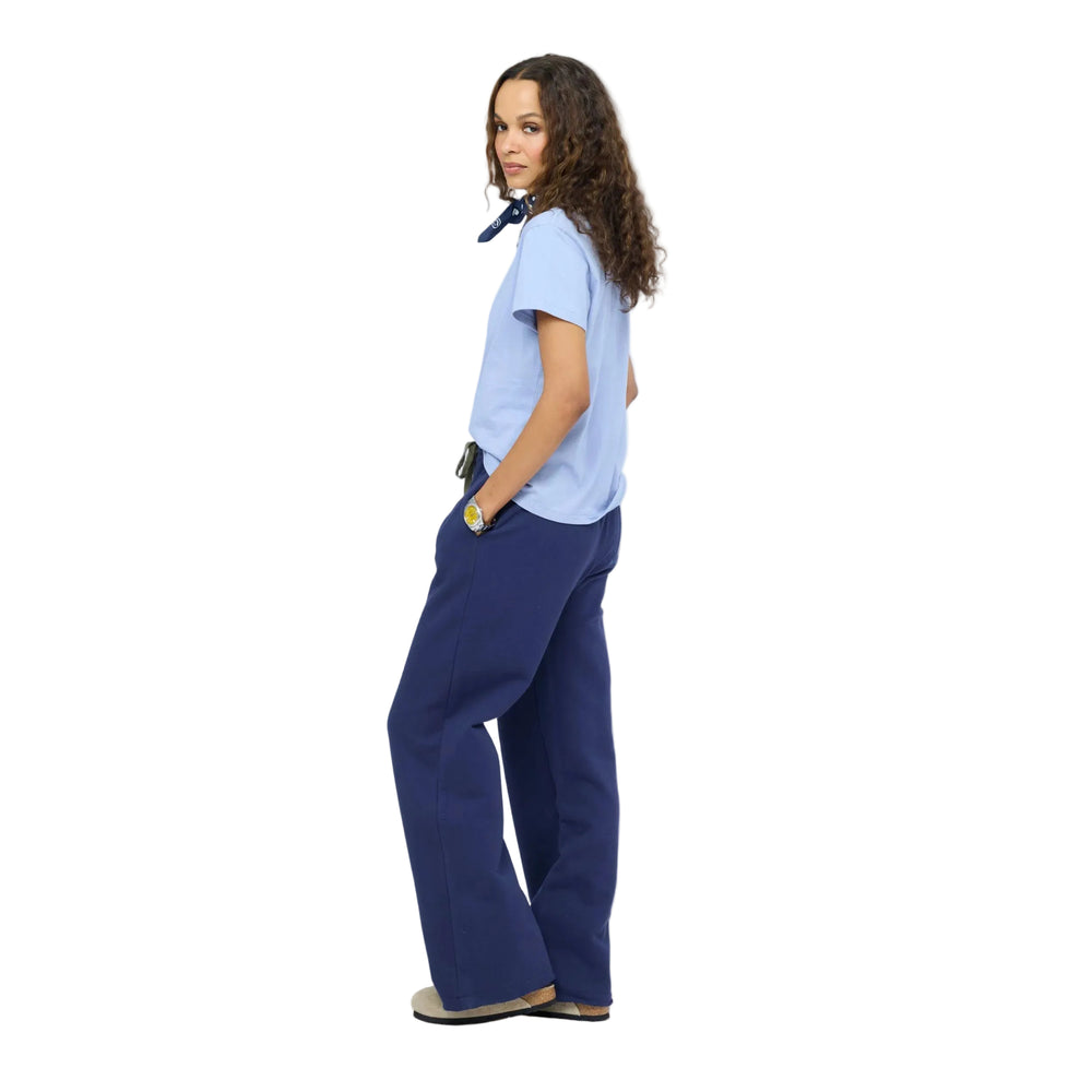 Side view of woman wearing  navy sweatpants, taupe slip-on shoes, and a brown baseball cap with a light blue heart, gold layered necklaces. Shop Kerri Rosenthal sweats.
