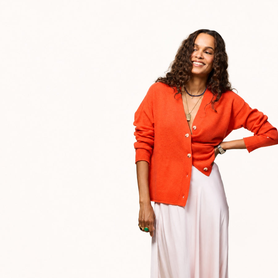 Woman wearing a tomato cardigan with a gold jewelery, natural white drawstring pants, and tomato heels.