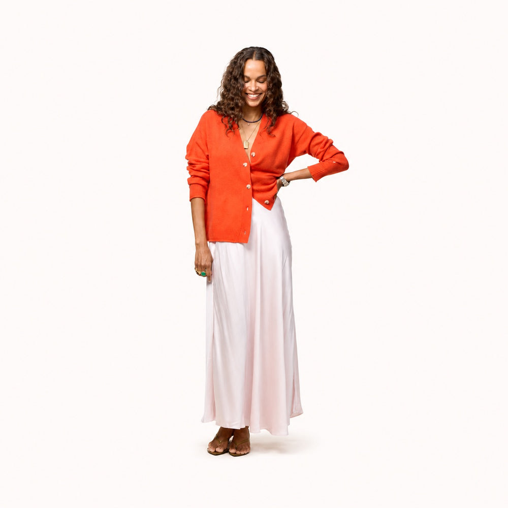 Woman wearing a tomato cardigan with a gold jewelery, natural white drawstring pants, and tomato heels.