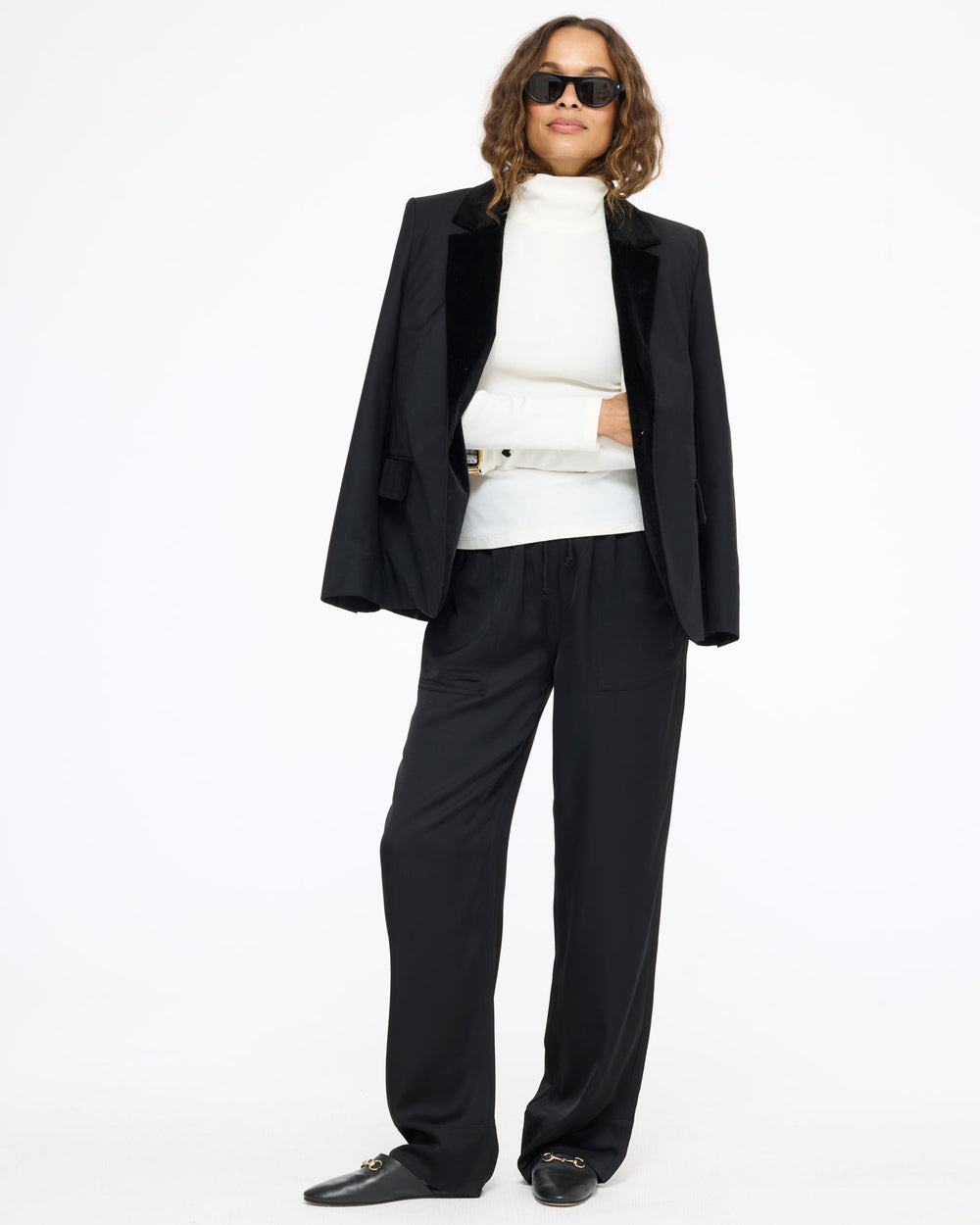 Model wearing the Mock Neck Rib Tee in cream under the Workday Fancy Blazer in black with the Coast Pant in black and sunglasses, front view