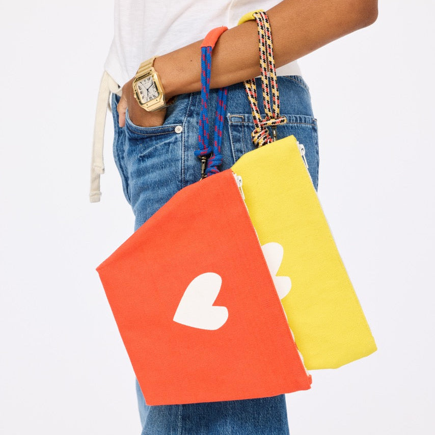 Person holding two colorful pouches with a heart design, wearing a white shirt and blue jeans.