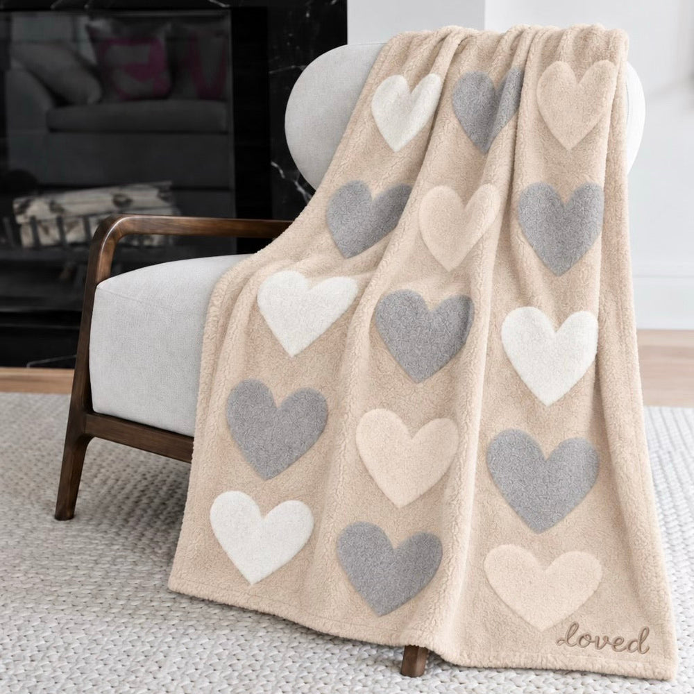 Doze Magoze blanket in cream with gray and white hearts draped over an armchair in a living room