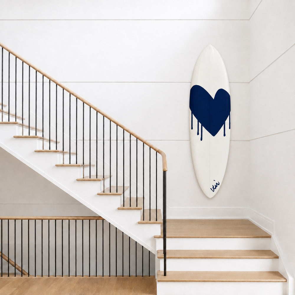 Kerri Rosenthal navy heart surfboard displayed on a wall above a wooden staircase