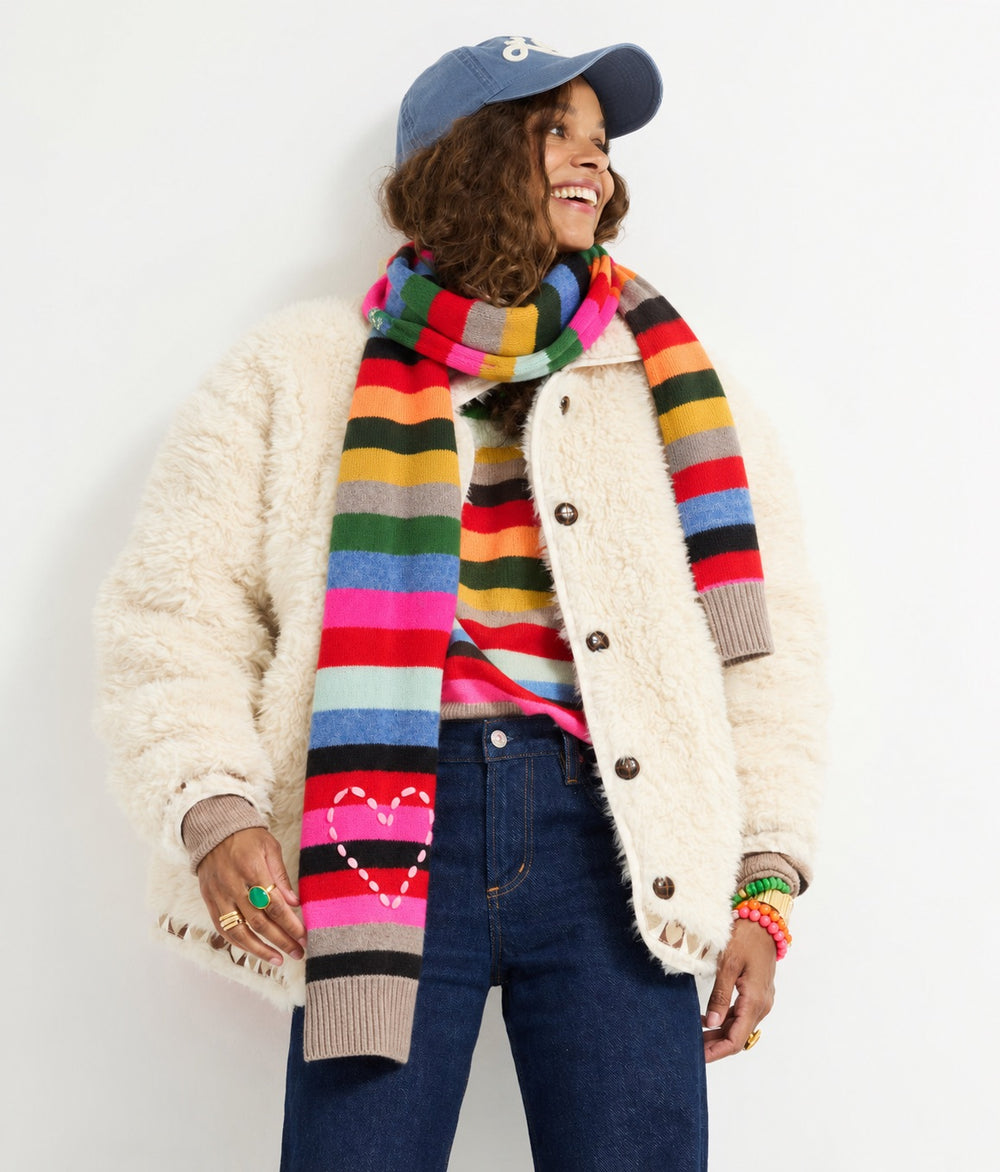 Model wearing the Fireside Scarf in multicolor stripe with the Cloud Nine Jacket in cream, the Loved Baseball Hat, the Patchwork Pullover Stripe Sweater, and jeans
