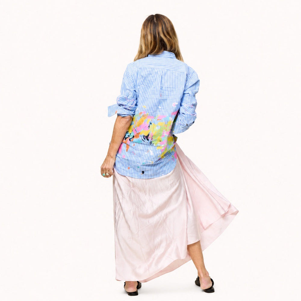 Back view of woman wearing an open blue striped shirt with colorful art print by artist Kerri Rosenthal, and pink maxi skirt