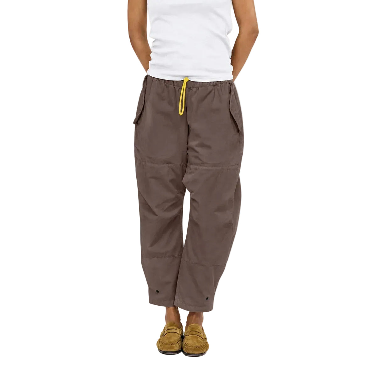 Close-up of a model wearing the Love Brigade Pant in brown with a yellow drawcord, a white tank top, and tan shoes, waist-down front view