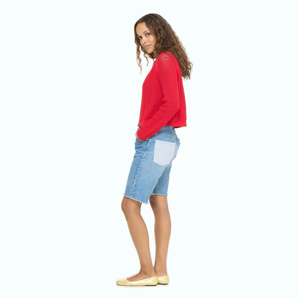 Woman wearing a red sweater and blue denim shorts on a white background