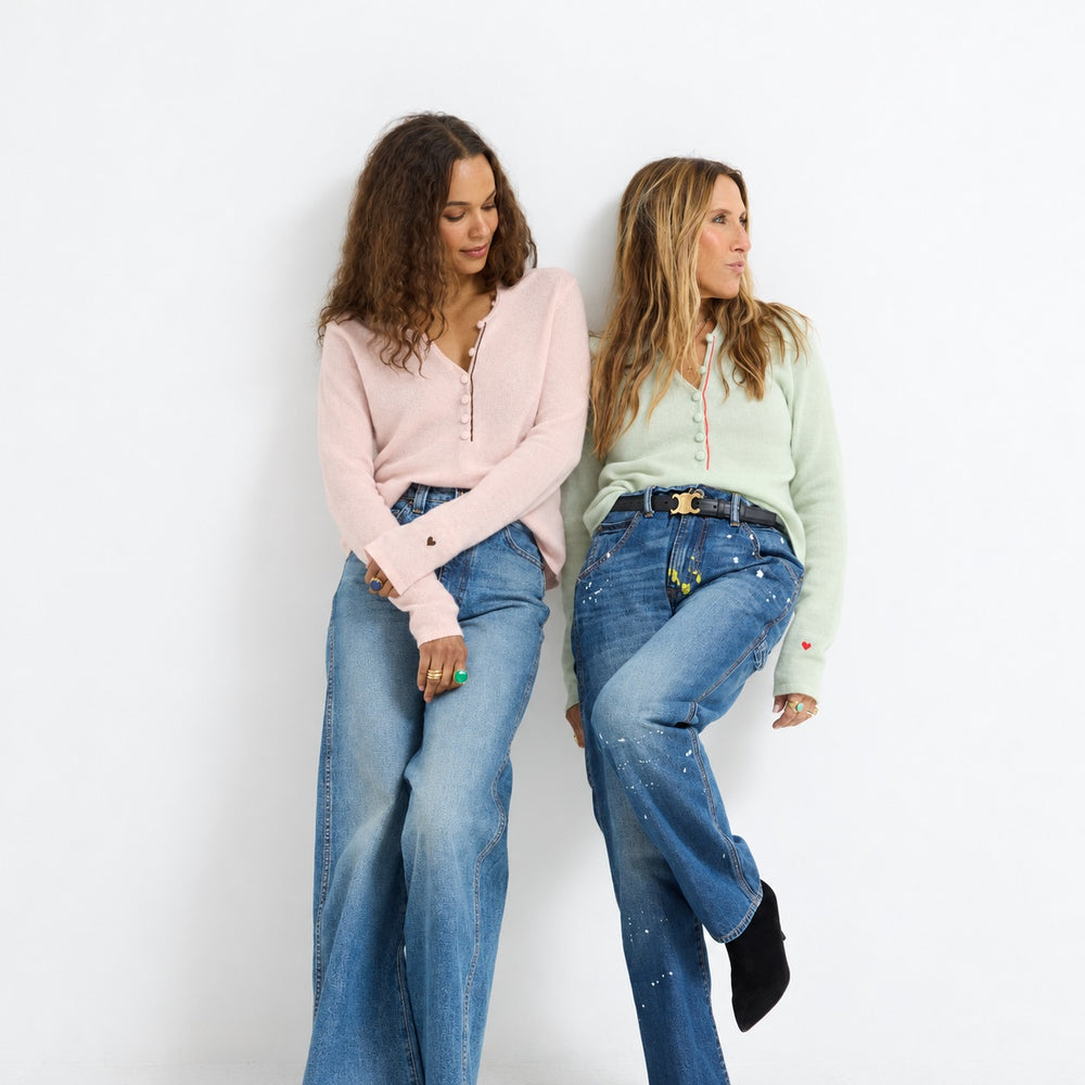 Two women leaning together in wide-leg jeans, one wearing the Pixie Sweater in pink and the other the Pixie Sweater in pistachio