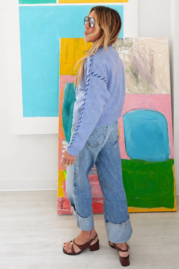 Model walking sideways in the Kerri Rosenthal blue cardigan, white top,  denim jeans.