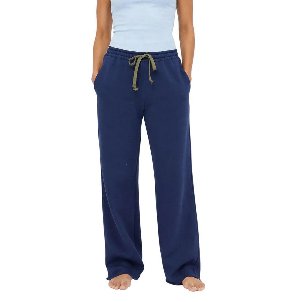 Close-up of a woman's lower half wearing Kerri Rosenthal navy wide-leg sweatpants with an olive drawstring, paired with a light blue t-shirt, taupe slip-on shoes, and layered rings and a bracelet.