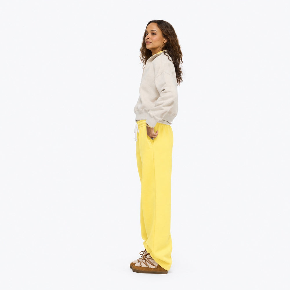 Model wearing the Weekend Barb Sweatpant in washed sunshine yellow with an oatmeal sweatshirt and sneakers, full length side view
